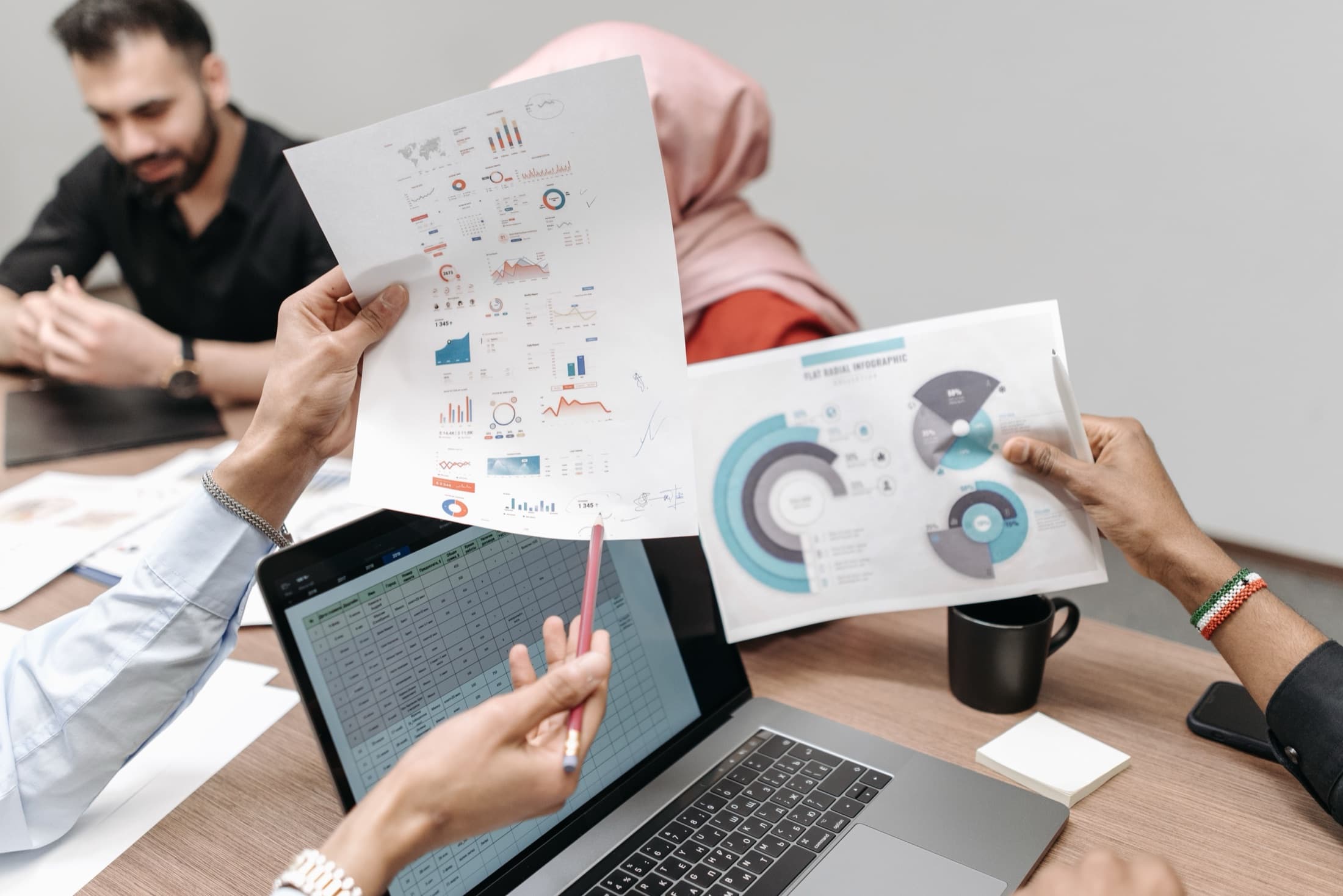 Colleagues comparing printed marketing reports beside a laptop
