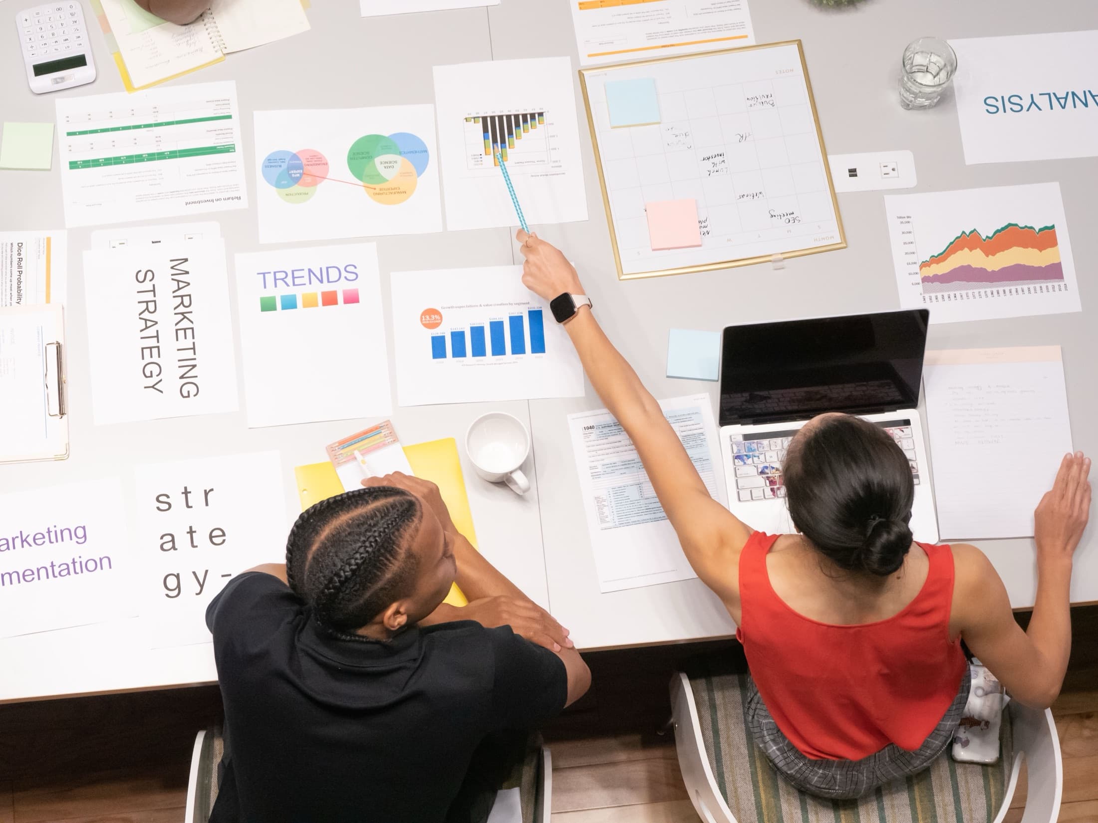 Overhead view of two people reviewing marketing charts and reports at a shared table